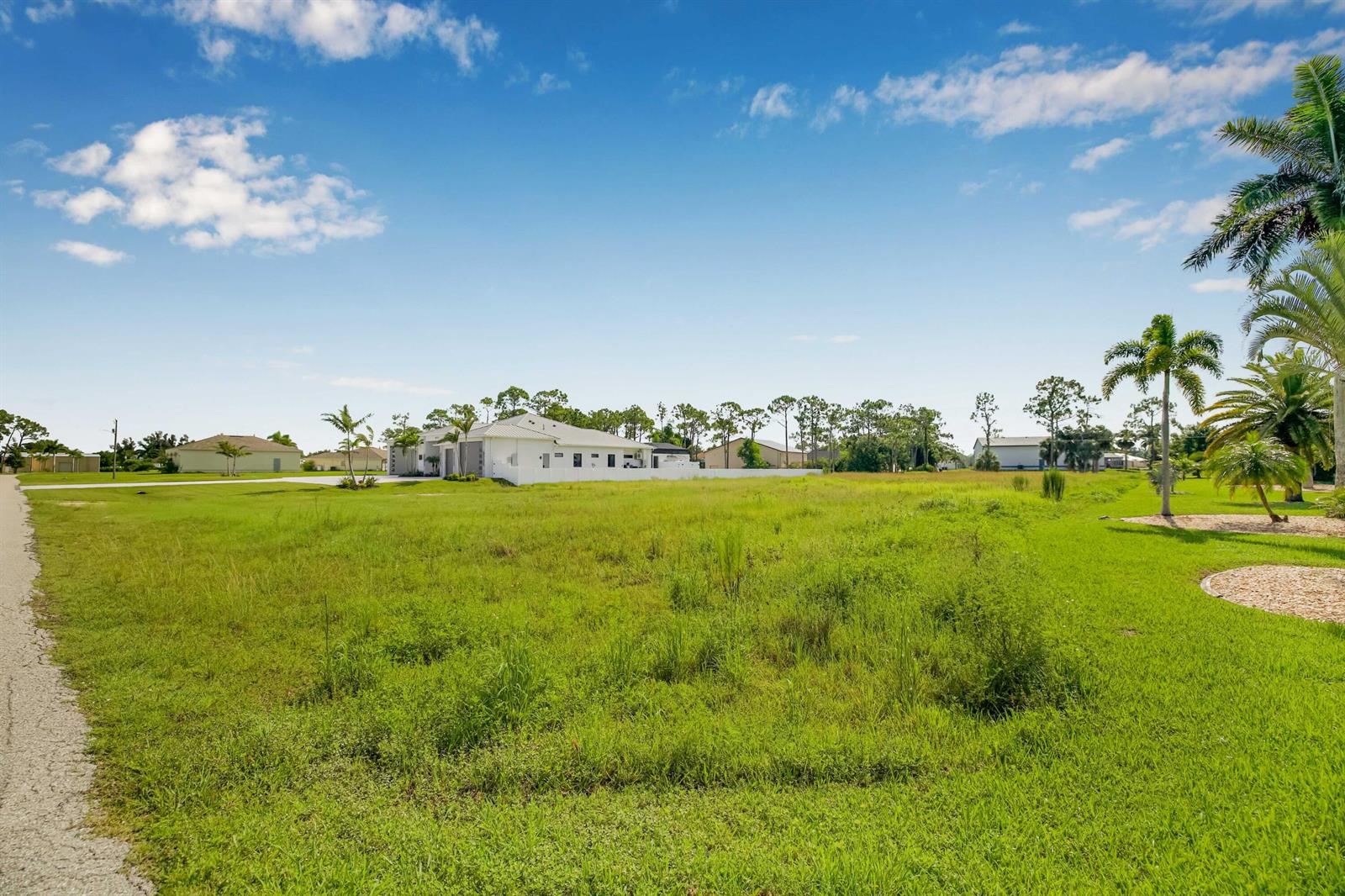 A large, grassy vacant lot sits in front of a modern white house under blue skies — 18742 Crosswind Avenue, FL 33917, FL