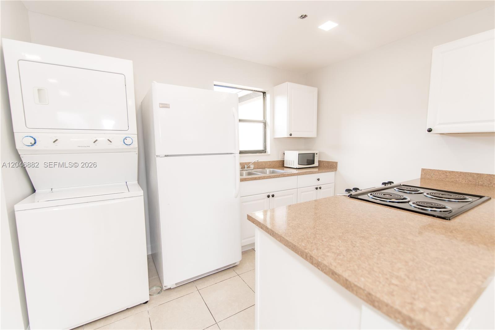 A kitchen features white cabinetry, tan countertops, a stacked washer-dryer unit, and white appliances — 1804 My Pl, West Palm Beach FL 33417, WEST PALM BEACH, FL