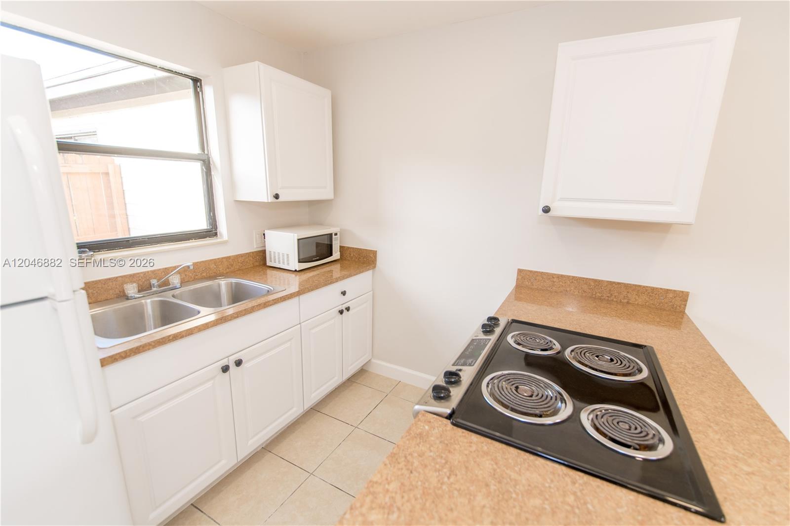 A kitchen features white cabinets, tan countertops, a double sink, and an electric stove — 1804 My Pl, West Palm Beach FL 33417, WEST PALM BEACH, FL