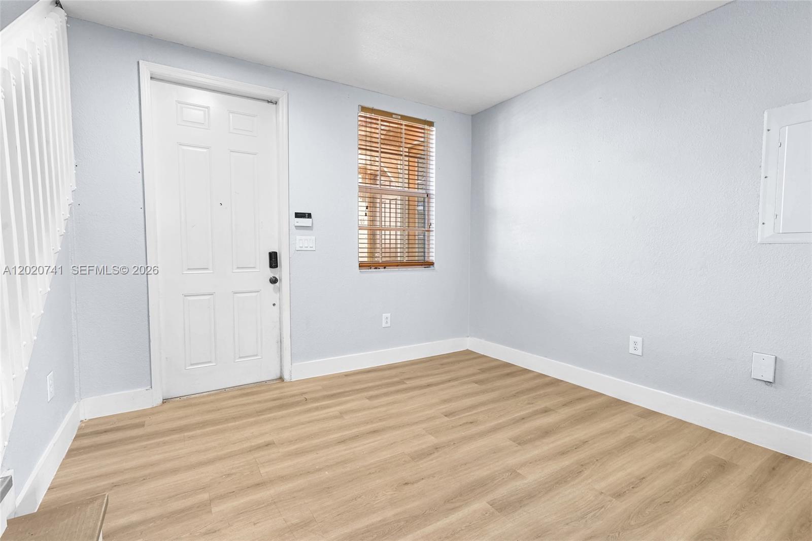 An empty room features light-colored walls, wood-look flooring, a white door, and a window — 1595 NE 33rd Rd # 3, Homestead FL 33033, HOMESTEAD, FL