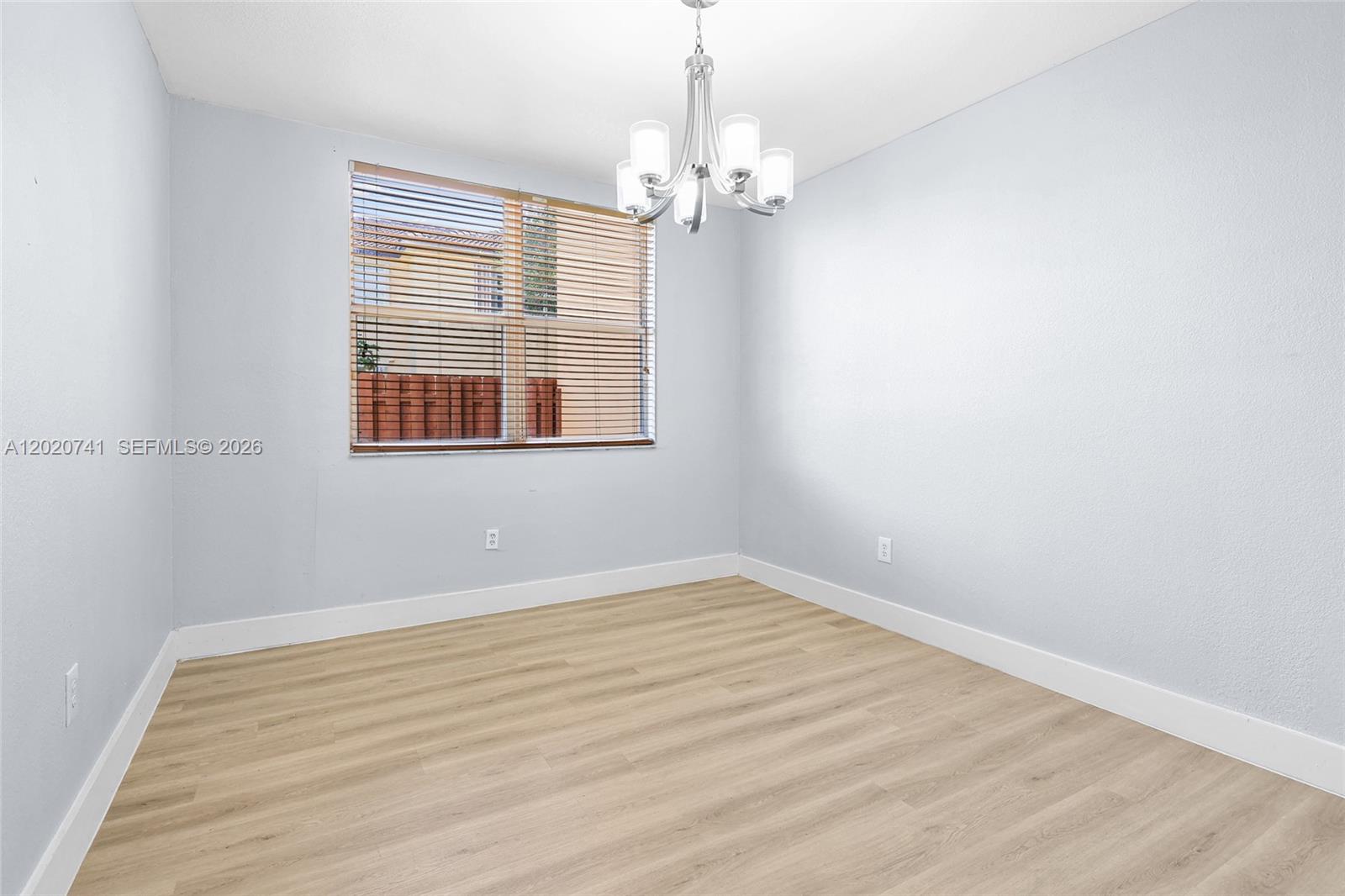 An empty room features light-colored wood-look flooring, pale blue walls, and a modern chandelier — 1595 NE 33rd Rd # 3, Homestead FL 33033, HOMESTEAD, FL