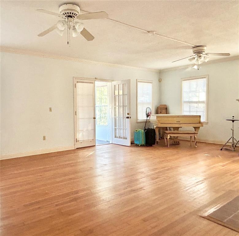 A spacious room with hardwood floors, two ceiling fans, a white piano, and French doors — 1105 HERNDON STREET, LEESBURG, FL