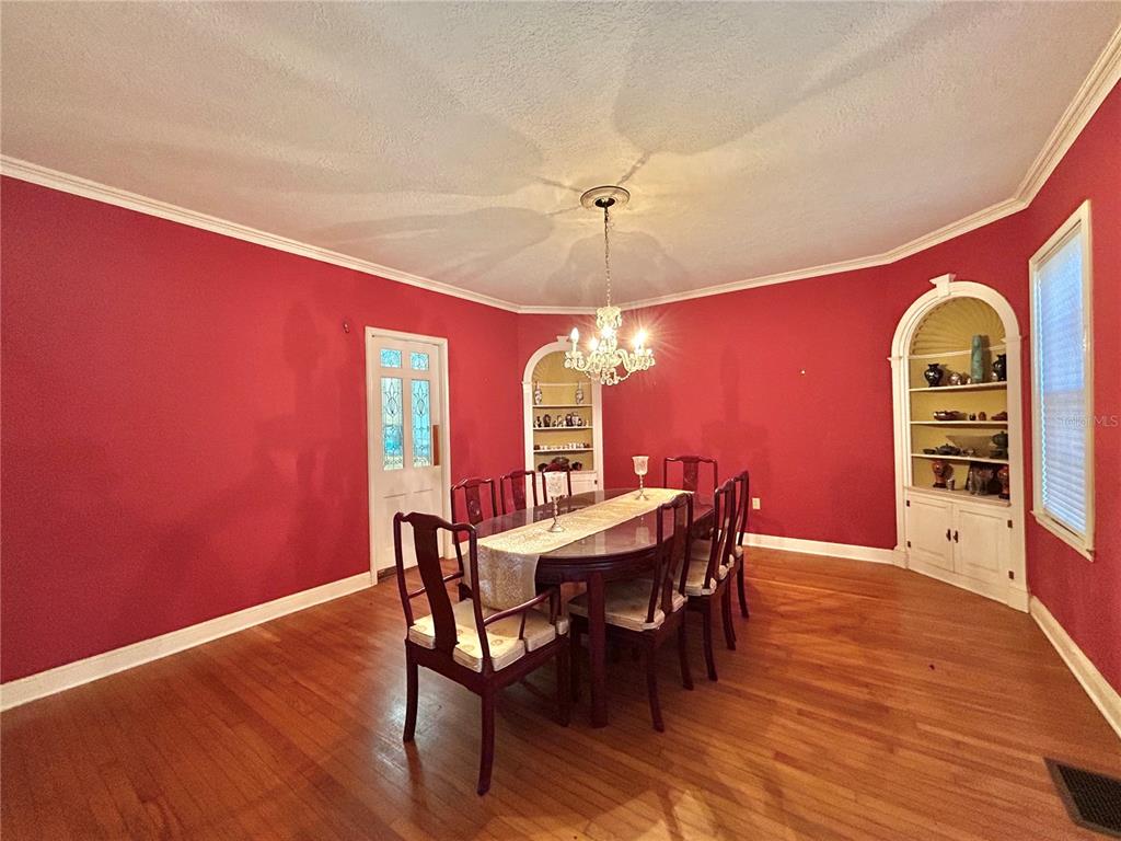 A formal dining room features red walls, hardwood floors, a chandelier, and two built-in cabinets — 1105 HERNDON STREET, LEESBURG, FL