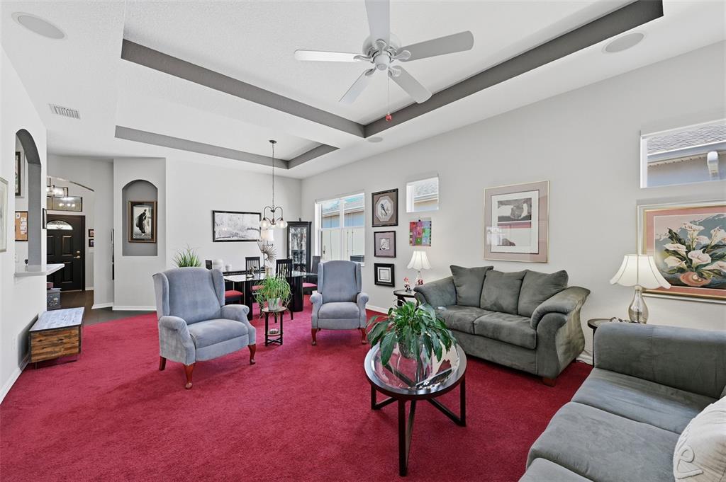 A living room features a red carpet, gray furniture, and a tray ceiling with a fan — 441 NOBLE FAIRE DRIVE, SUN CITY CENTER, FL