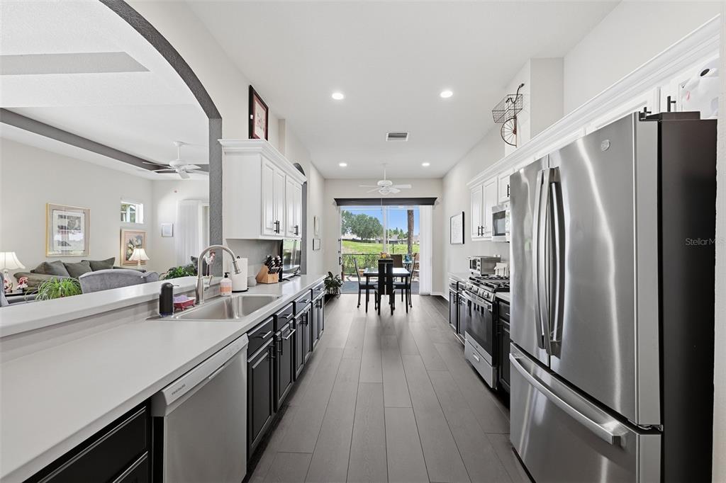 A modern kitchen features dark lower cabinets, white upper cabinets, stainless steel appliances, and wood-look flooring — 441 NOBLE FAIRE DRIVE, SUN CITY CENTER, FL
