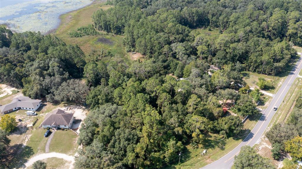 An aerial view shows a wooded lot with two houses near a lake and road — 101 ASHLEY LAKE DRIVE, MELROSE, FL