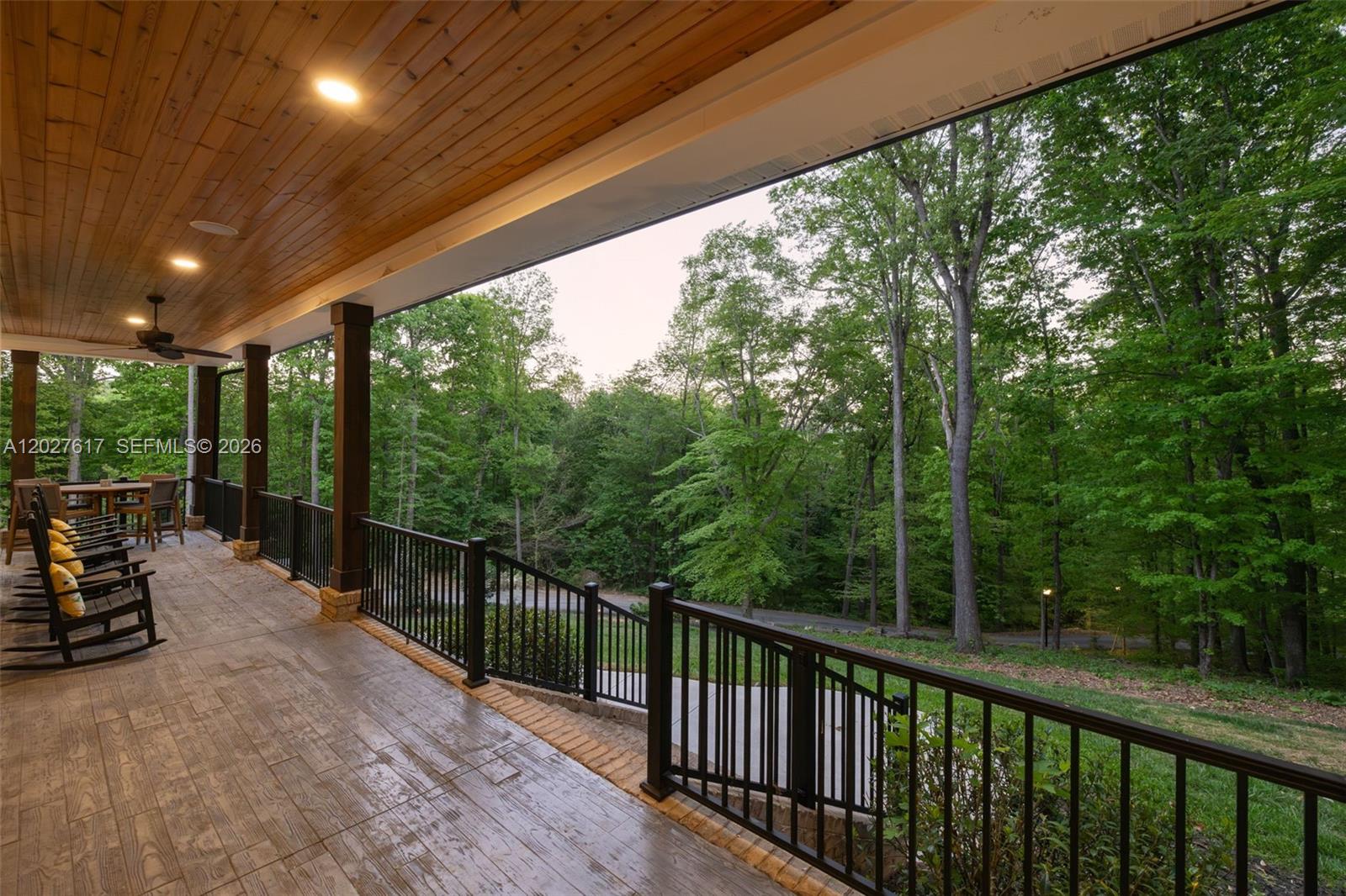 A covered wooden deck features rocking chairs, black railings, and a view of trees — 1642 Pineview Road, NC 27317, NC