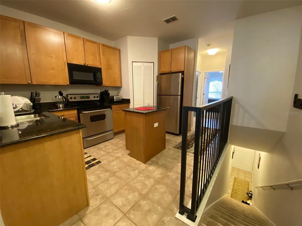 A kitchen with wood cabinets, stainless steel appliances, and a small island overlooks a staircase — 2261 TUSCANY TRACE UNIT 106, PALM HARBOR, FL