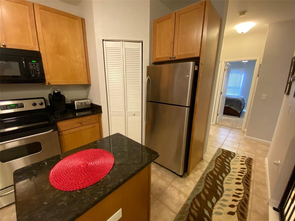 A kitchen features stainless steel appliances, dark countertops, wood cabinetry, and a small island — 2261 TUSCANY TRACE UNIT 106, PALM HARBOR, FL