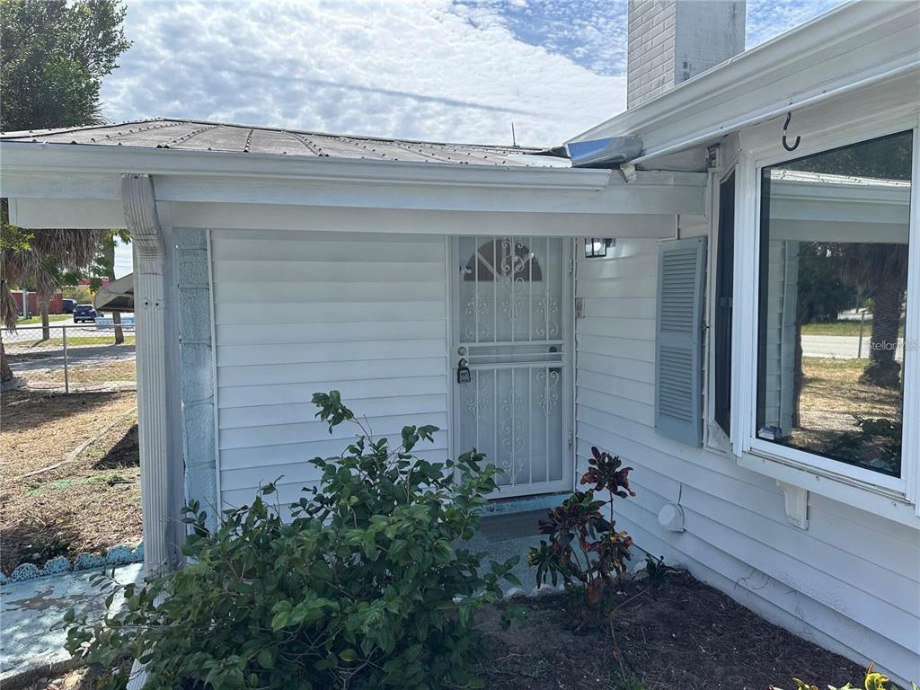 A white house exterior features a metal security screen door and a large bay window — 9741 SCENIC DRIVE, PORT RICHEY, FL