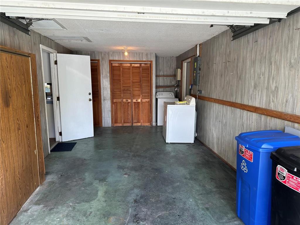 A garage with wood-paneled walls, a concrete floor, laundry appliances, and several doors — 9741 SCENIC DRIVE, PORT RICHEY, FL