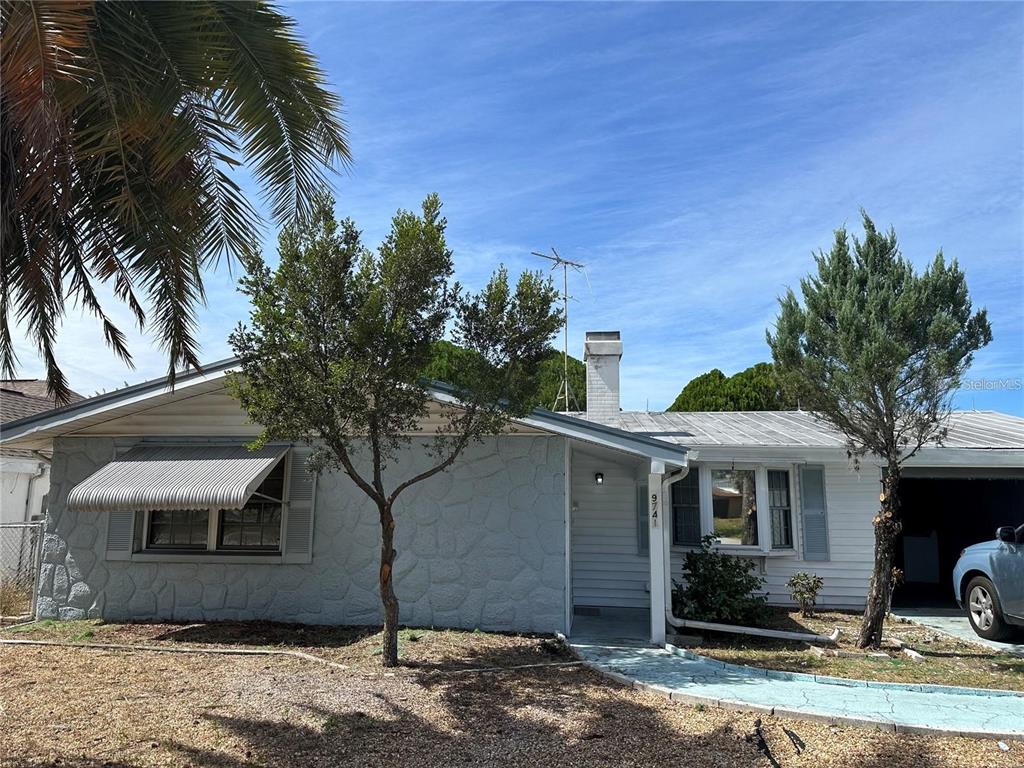 A single-story house with a white stone facade, metal roof, and a palm tree — 9741 SCENIC DRIVE, PORT RICHEY, FL