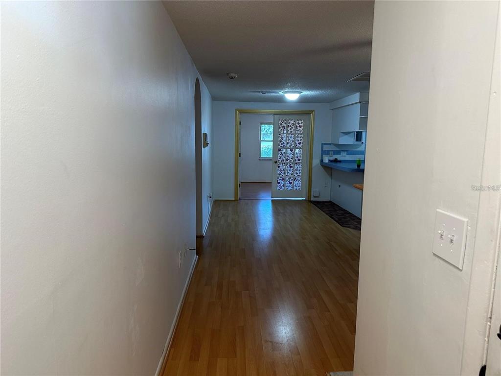 A view from a hallway looking into a living area with wood-look flooring and kitchen — 9741 SCENIC DRIVE, PORT RICHEY, FL