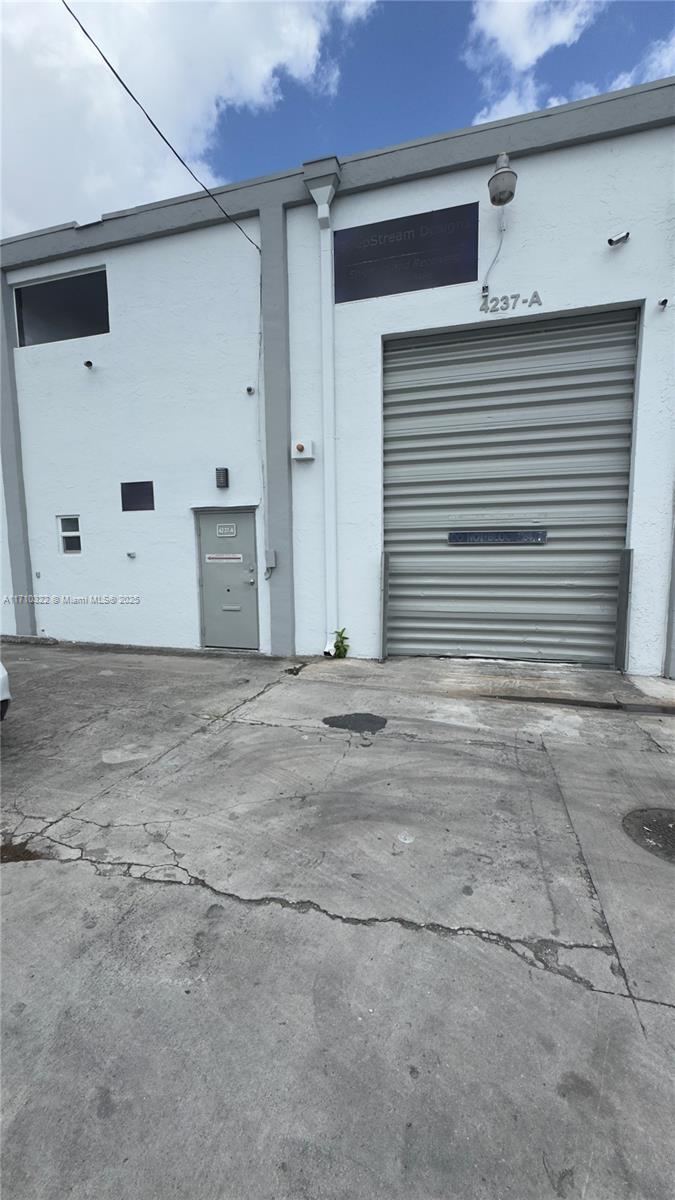 An exterior view of a commercial warehouse building with a roll-up door and pedestrian entrance — 4201 NW 37th Ave # A, Miami FL 33142, MIAMI, FL