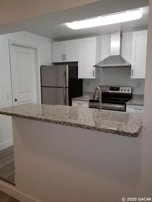 A kitchen features white cabinets, stainless steel appliances, and a granite-topped breakfast bar — 1115 NE 5TH PLACE, GAINESVILLE, FL
