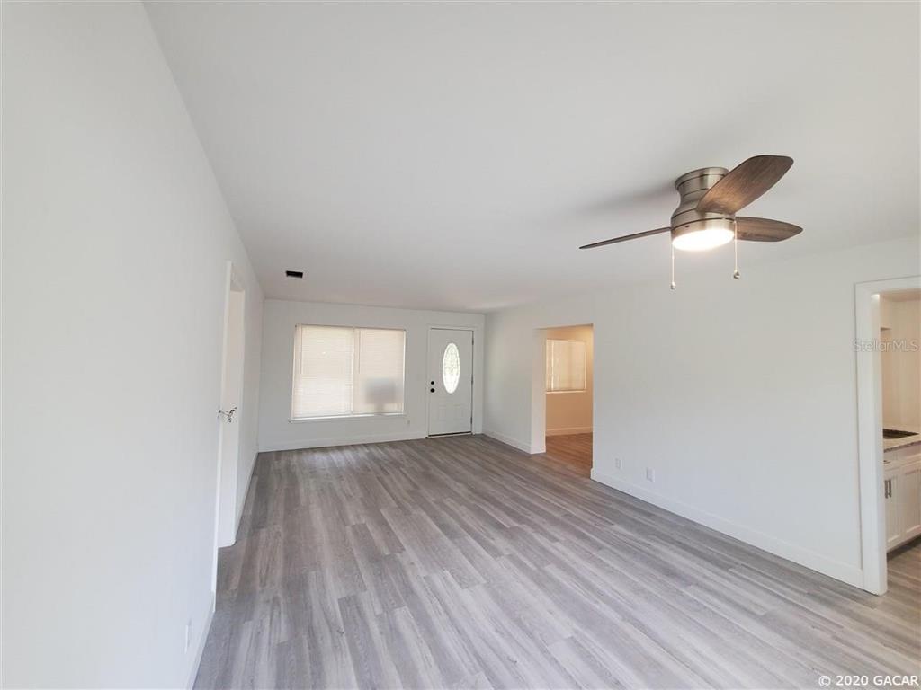 An empty living room features white walls, light wood-look flooring, and a ceiling fan — 1115 NE 5TH PLACE, GAINESVILLE, FL
