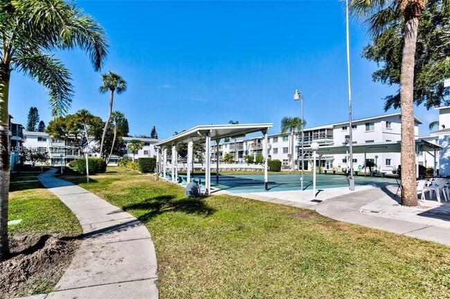 A paved walkway leads toward a covered outdoor pavilion situated between multi-story apartment buildings — 1832 Sunny Drive # 32, Bradenton FL 34207, BRADENTON, FL