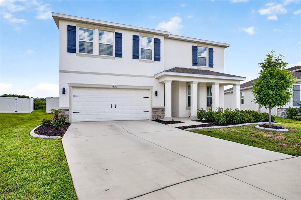 A two-story suburban house with a white stucco exterior, blue shutters, and a concrete driveway — 13793 WINEBERRY DRIVE, DADE CITY, FL