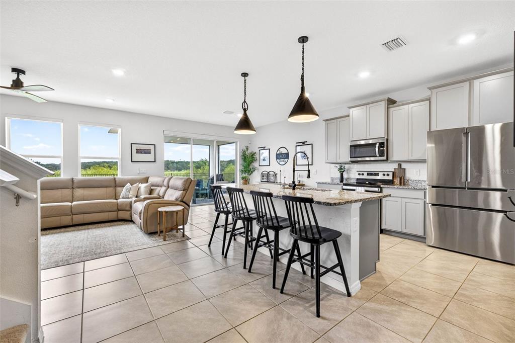 An open-concept kitchen and living area featuring light gray cabinetry, granite countertops, and tile flooring — 13793 WINEBERRY DRIVE, DADE CITY, FL