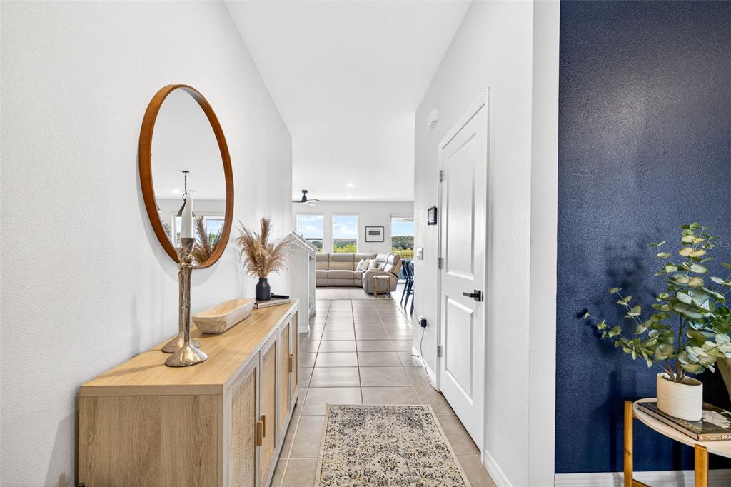 A hallway with a wooden console table, round mirror, and tile flooring leads to a living area — 13793 WINEBERRY DRIVE, DADE CITY, FL