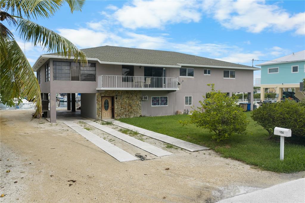 An elevated two-story house with a stone-accented entrance, a balcony, and a gravel driveway — 2100 AVENUE H, MARATHON, FL