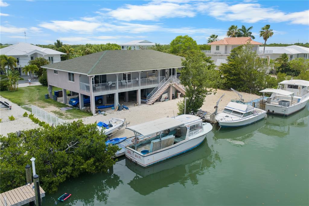 An elevated house sits on a waterfront lot with several boats docked in the canal — 2100 AVENUE H, MARATHON, FL