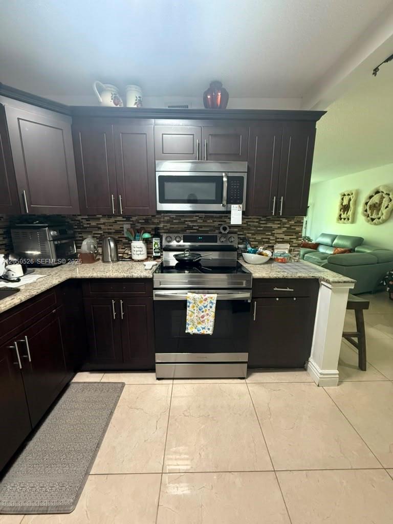 A kitchen features dark wood cabinets, stainless steel appliances, and a tiled backsplash — 9405 W Flagler St # 212D, Miami FL 33174, MIAMI, FL