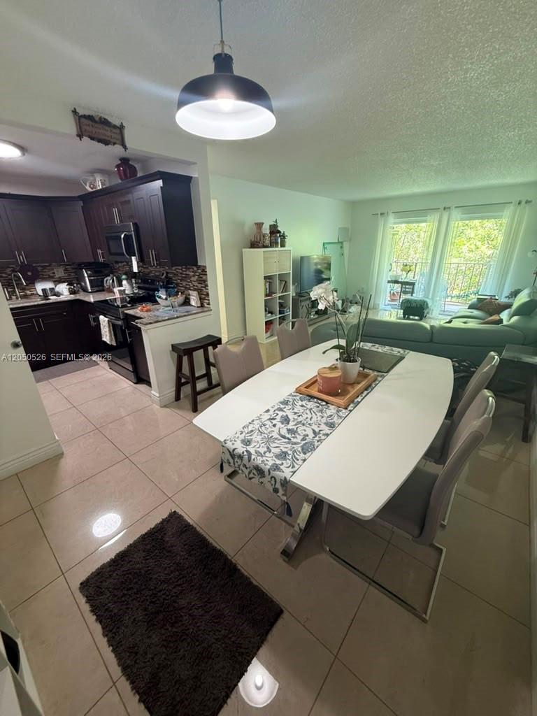 An open-concept dining area features a white table, tile flooring, and an adjacent kitchen — 9405 W Flagler St # 212D, Miami FL 33174, MIAMI, FL