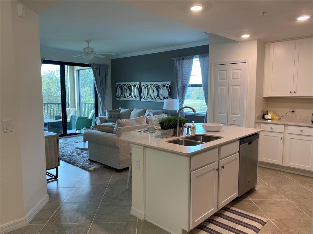 An open-concept kitchen with a white island overlooks a living room with a balcony view — 17510 GAWTHROP DRIVE UNIT 208, BRADENTON, FL
