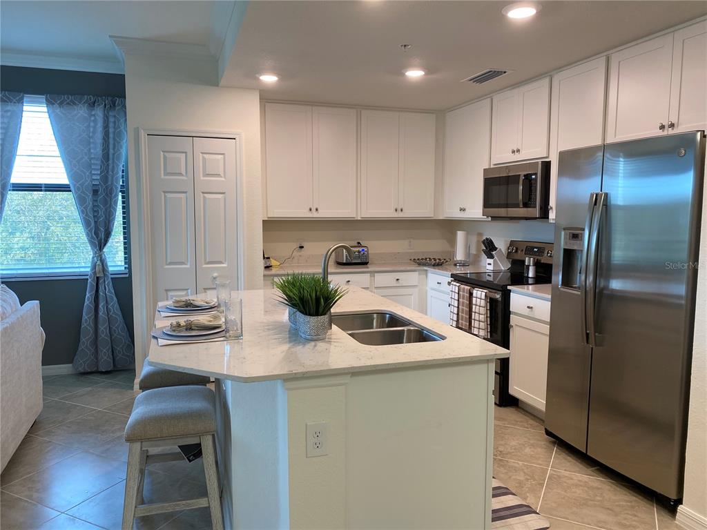A kitchen features white cabinets, stainless steel appliances, and a central island with a sink — 17510 GAWTHROP DRIVE UNIT 208, BRADENTON, FL