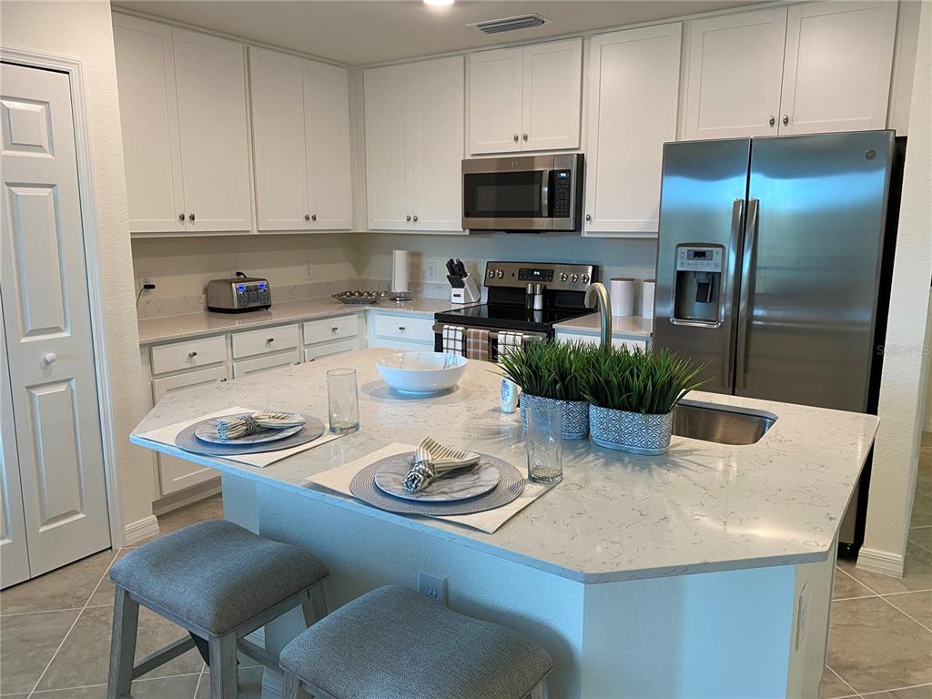 A kitchen features white cabinets, stainless steel appliances, and a large central island with seating — 17510 GAWTHROP DRIVE UNIT 208, BRADENTON, FL