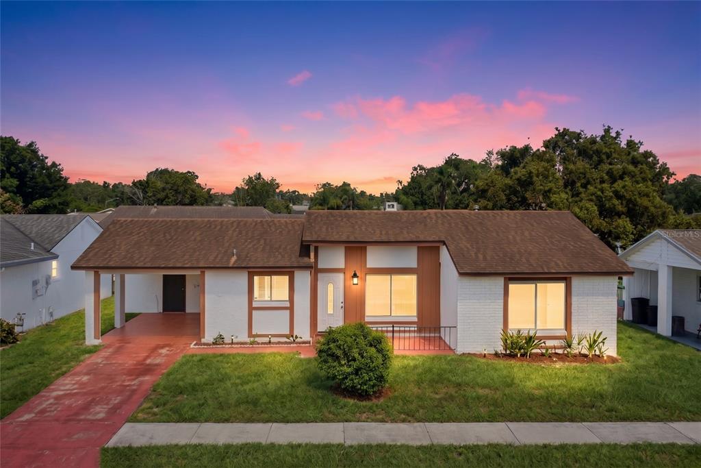 A single-story white brick house with a brown roof and a front carport at dusk — 10330 GALLIARD BOULEVARD, ORLANDO, FL
