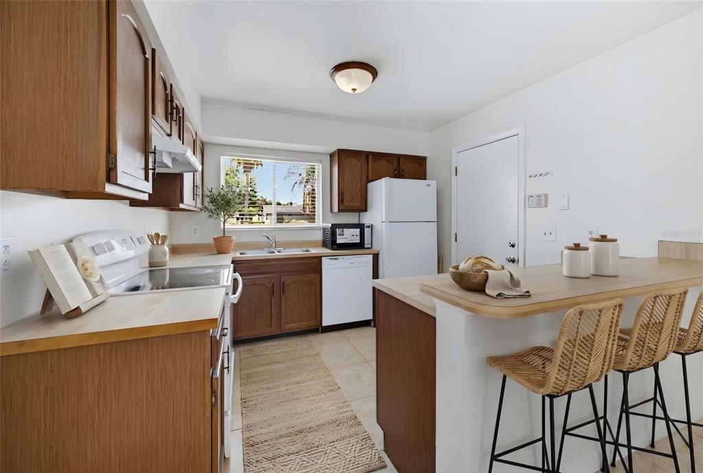 A kitchen features wood cabinets, white appliances, a breakfast bar, and a window over the sink — 10330 GALLIARD BOULEVARD, ORLANDO, FL