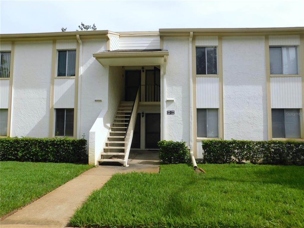 A two-story apartment building exterior features white stucco walls, tan trim, and an outdoor staircase — 105 PALMETTO COURT, OLDSMAR, FL