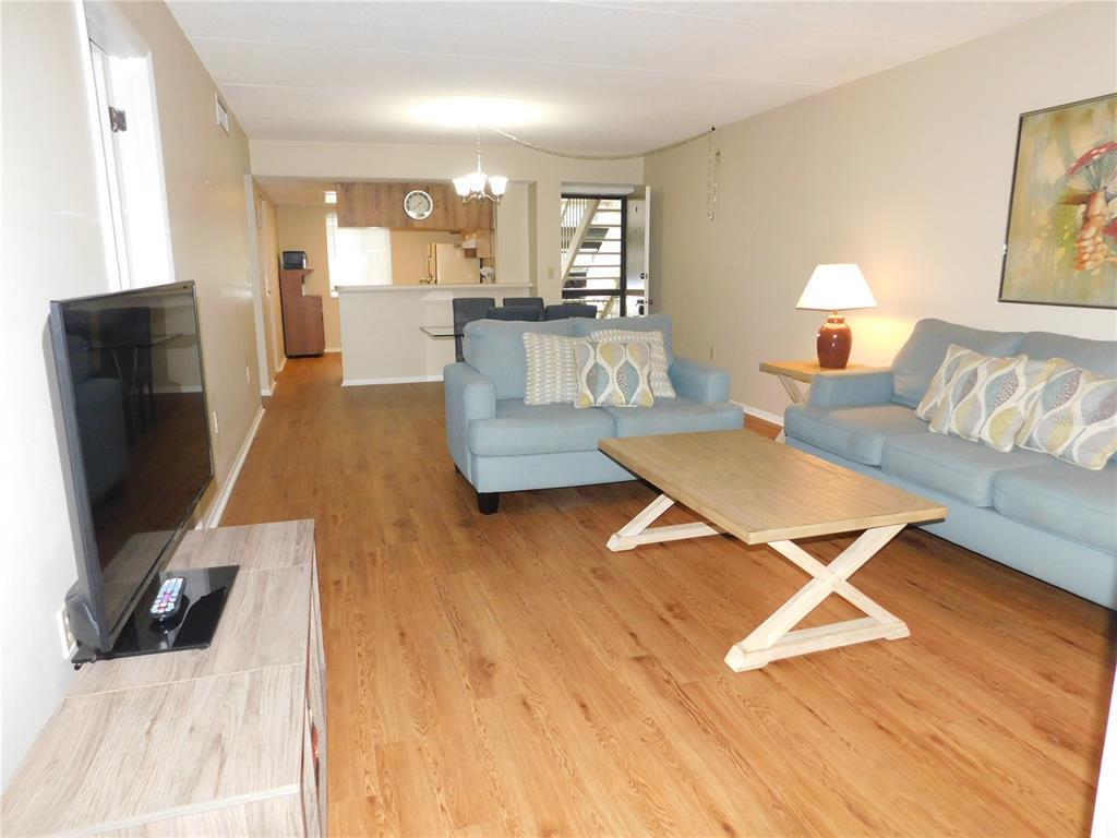 A living room with light wood flooring, two blue sofas, and an open kitchen area — 105 PALMETTO COURT, OLDSMAR, FL