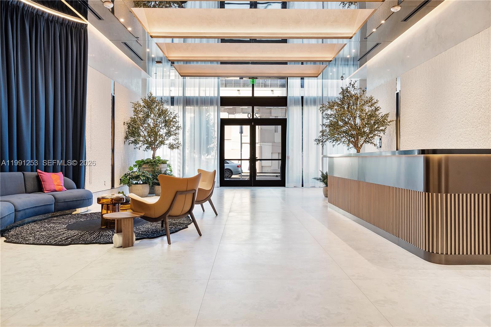 A modern lobby features a reception desk, blue sofa, two armchairs, and floor-to-ceiling windows — 20 NE 11th St # 3809, Miami FL 33132, MIAMI, FL