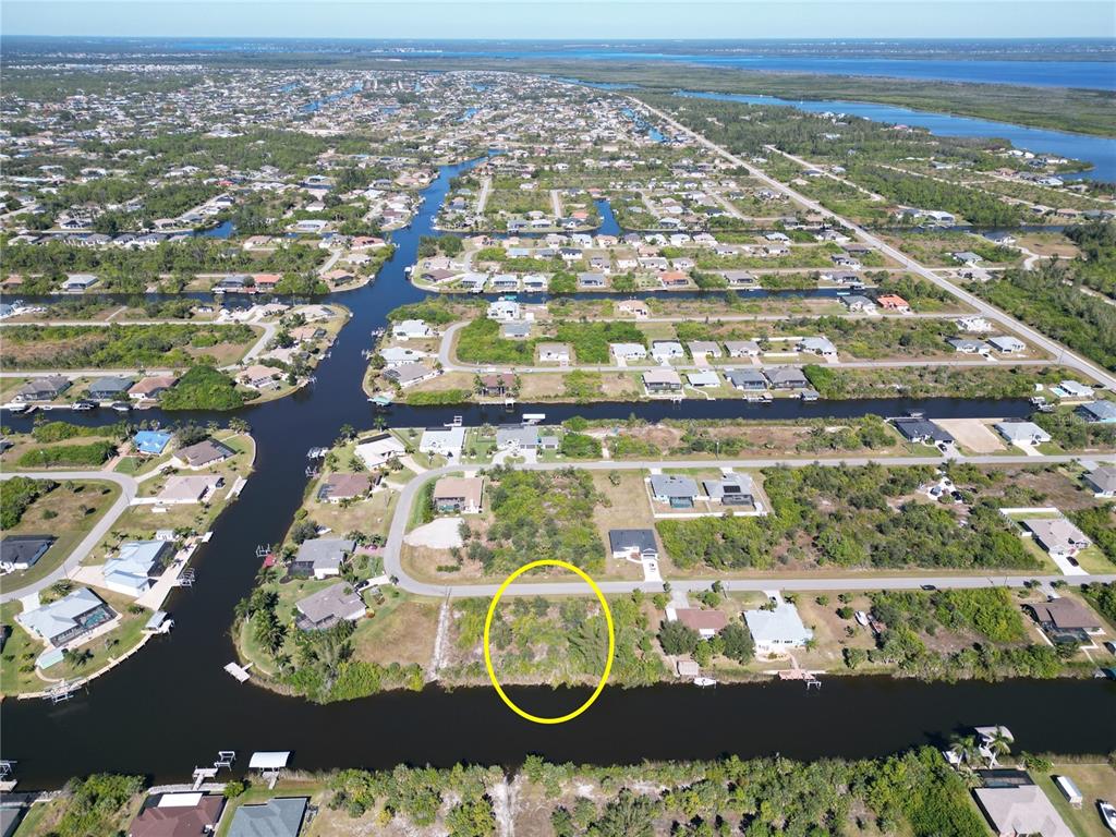 An aerial view shows a vacant, wooded waterfront lot highlighted by a yellow circle — 15706 STUART CIRCLE, PORT CHARLOTTE, FL