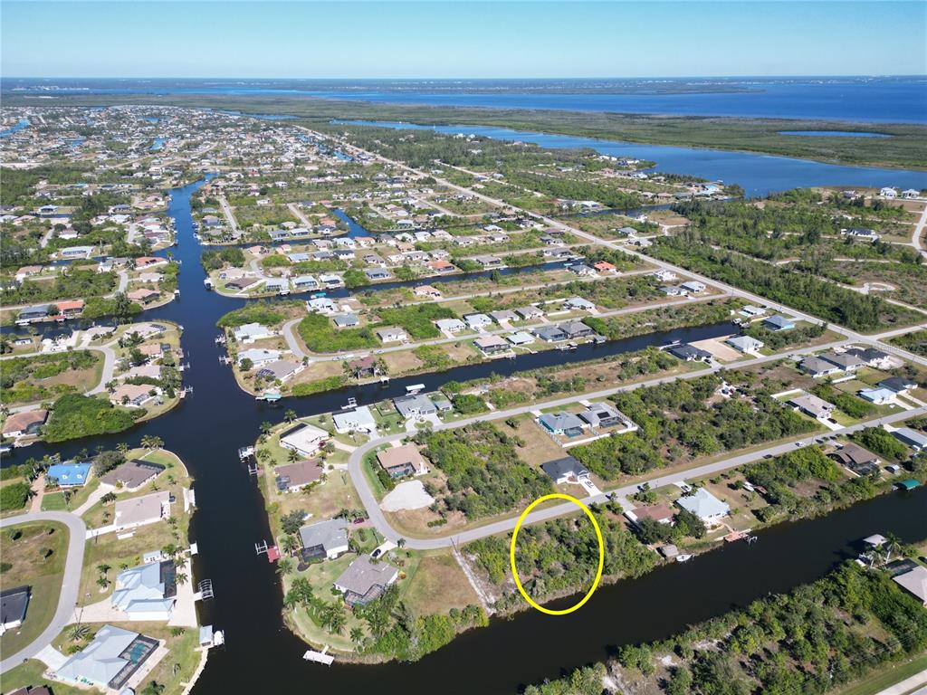 An aerial view shows a vacant, wooded waterfront lot highlighted by a yellow circle — 15706 STUART CIRCLE, PORT CHARLOTTE, FL