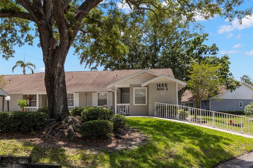 A single-story building with a wheelchair ramp leading to the entrance under a large tree — 1465 OAK HILL DRIVE UNIT 104, DUNEDIN, FL