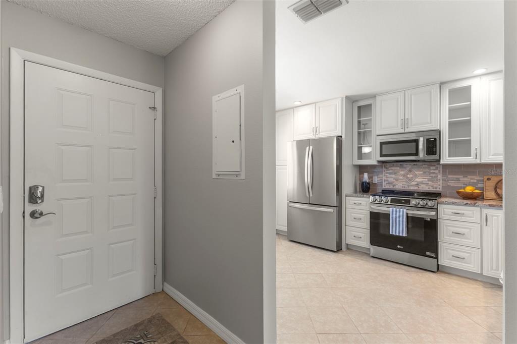 A covered porch with two chairs overlooks a sidewalk, a carport, and mature trees — 1465 OAK HILL DRIVE UNIT 104, DUNEDIN, FL