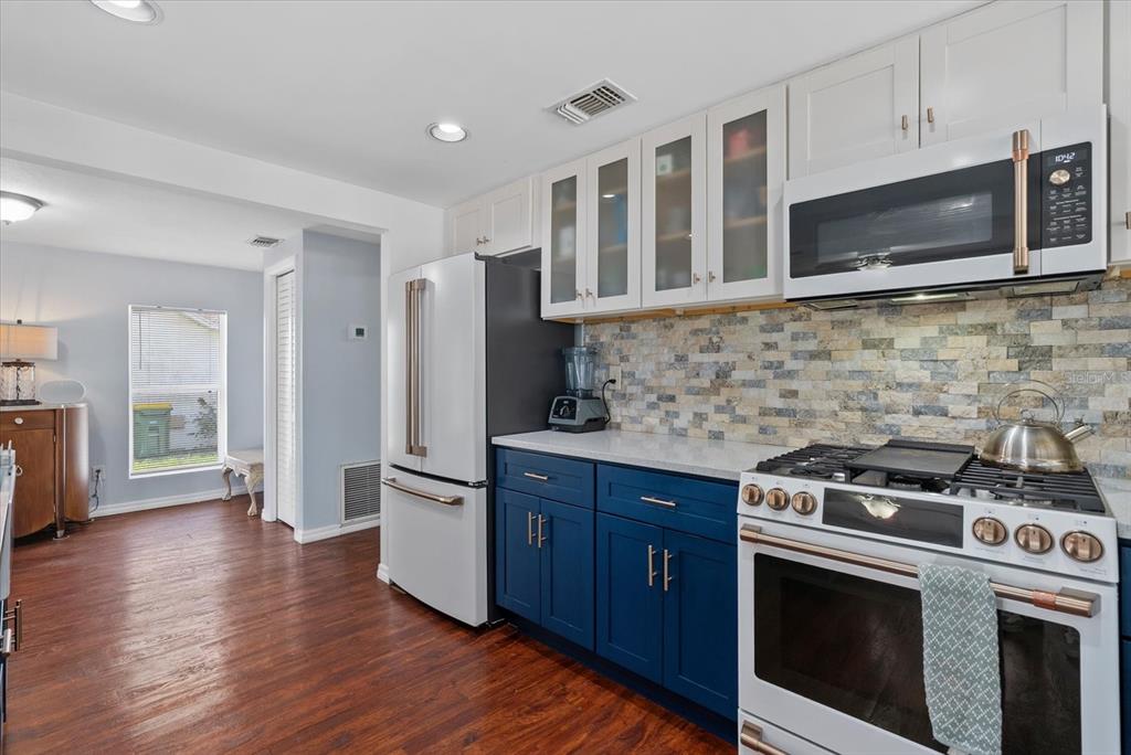 A kitchen features blue lower cabinets, white upper cabinets, a stone backsplash, and stainless appliances — 4111 SARASOTA AVENUE, SARASOTA, FL
