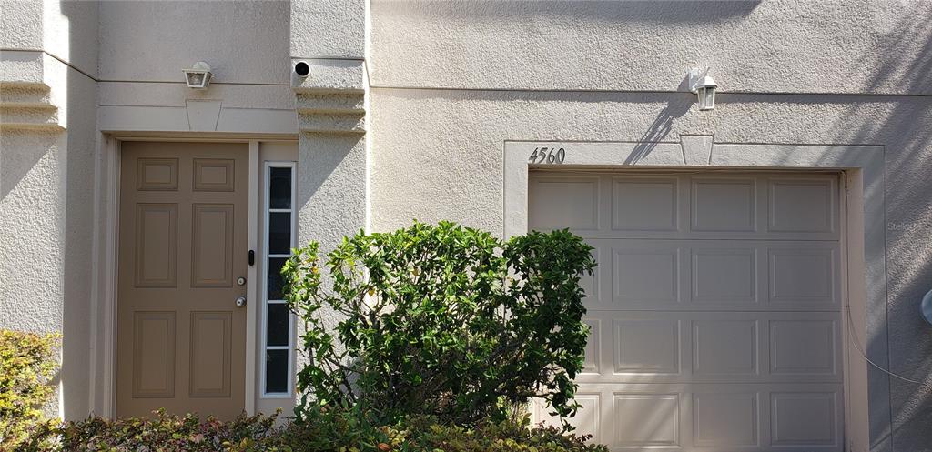 The exterior of a home features a tan front door, a garage, and a bush — 4560 ASHBURN SQUARE DRIVE, TAMPA, FL