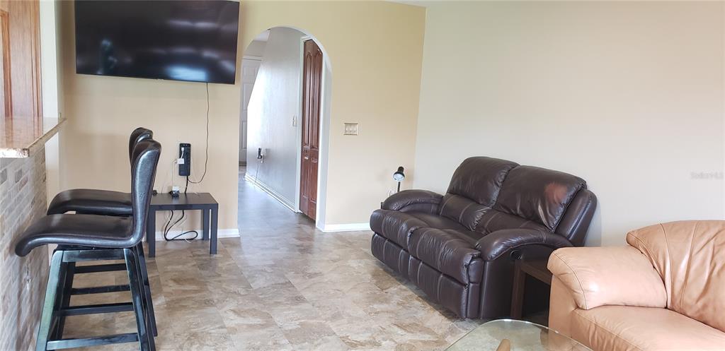 A living room features tiled floors, a dark leather loveseat, and a wall-mounted television — 4560 ASHBURN SQUARE DRIVE, TAMPA, FL