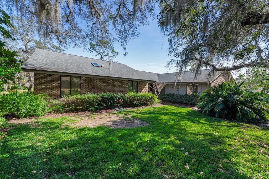 A brick house with a gray shingled roof sits behind a green lawn and trees — 507 BOXWOOD LANE, NEW SMYRNA BEACH, FL