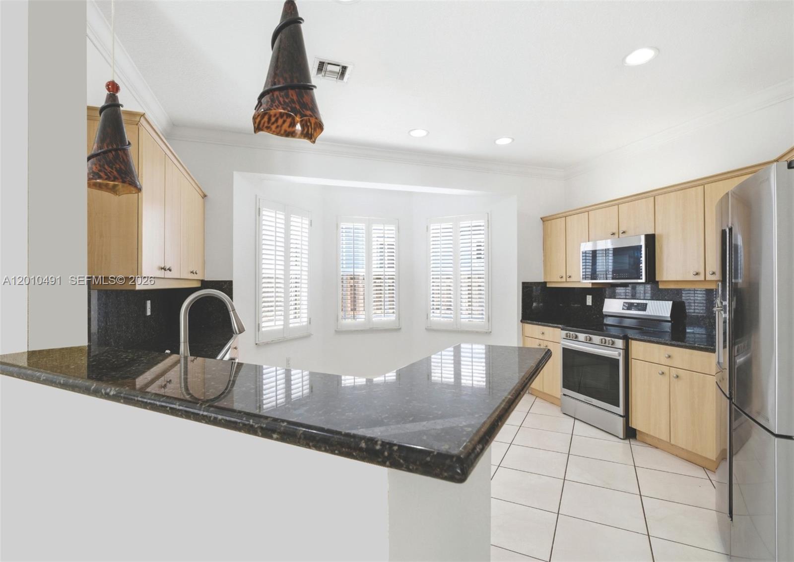 A kitchen features light wood cabinets, dark granite countertops, stainless steel appliances, and tile flooring — 15203 SW 142nd Ave, Miami FL 33177, MIAMI, FL