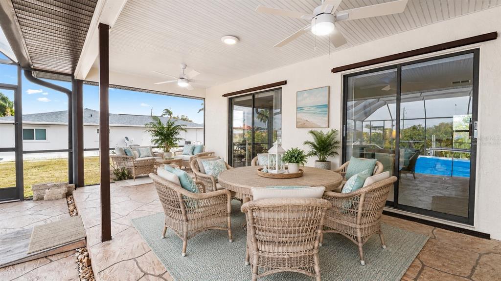 A covered patio features wicker furniture, a dining table, and sliding glass doors to a pool — 27248 SAN MARINO DRIVE, PUNTA GORDA, FL