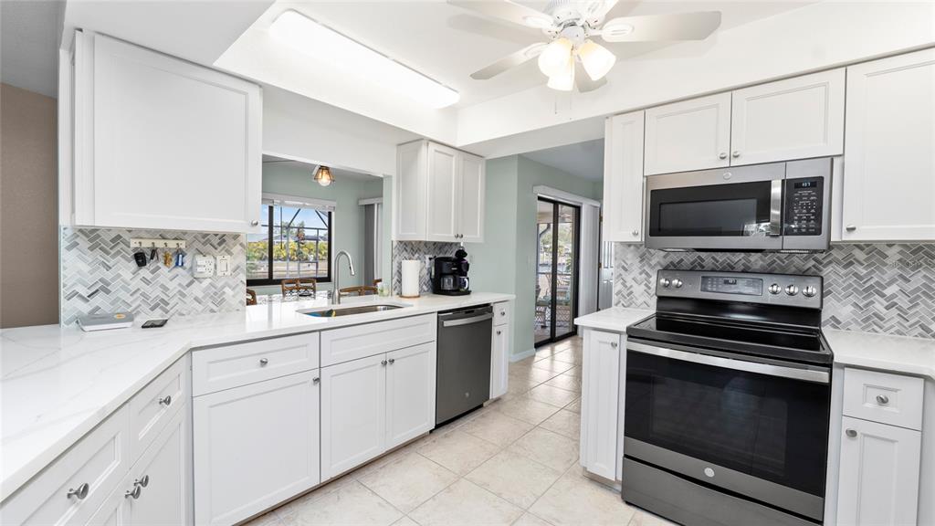 A kitchen features white cabinets, stainless steel appliances, quartz countertops, and a herringbone tile backsplash — 27248 SAN MARINO DRIVE, PUNTA GORDA, FL
