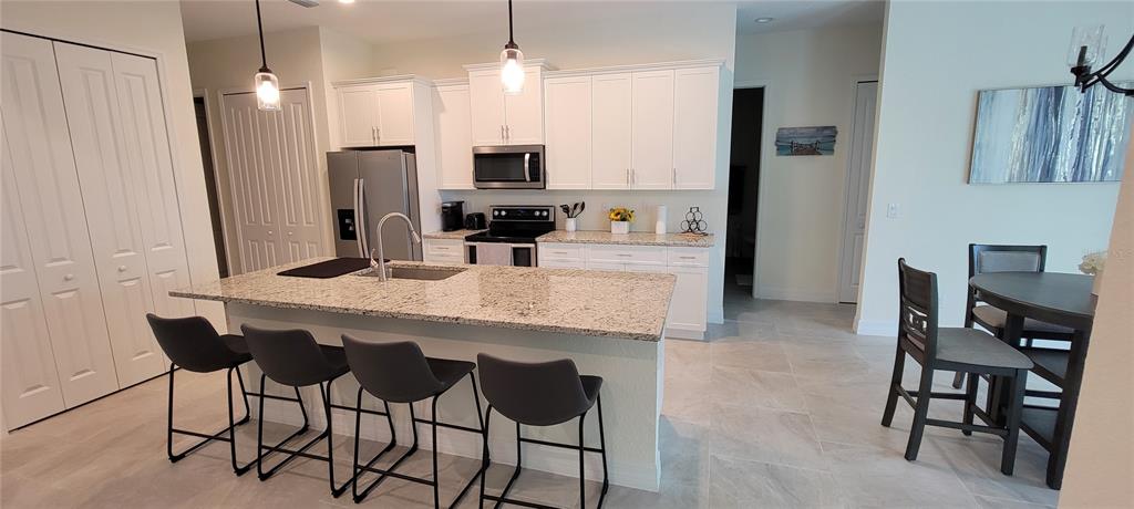 A kitchen features white cabinets, granite countertops, a center island with bar seating, and appliances — 13376 YAGER LANE, PORT CHARLOTTE, FL