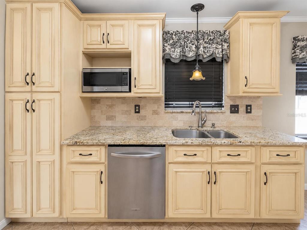A kitchen features cream-colored cabinets, granite countertops, a stainless steel dishwasher, and a window — 6286 SW 110TH STREET, OCALA, FL