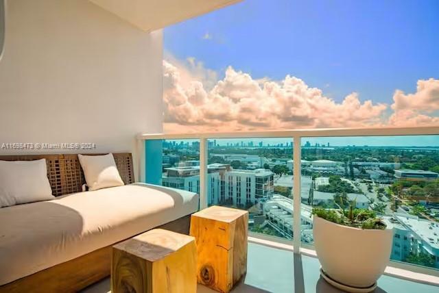 A balcony with a daybed, two wooden stools, a potted plant, and a city view — 102 24th St # 1021, Miami Beach FL 33139, MIAMI BEACH, FL